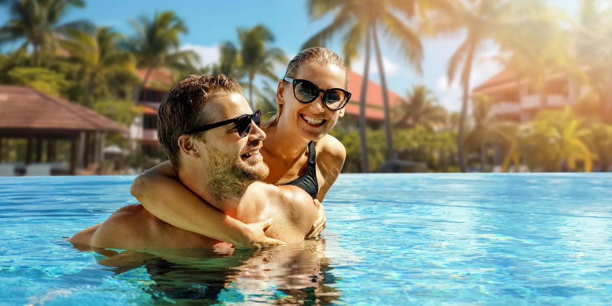 Couple wearing SUNVIBE® polarised sunglasses in a tropical swimming pool